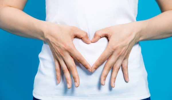 young woman who makes a heart shape by hands on her stomach.
